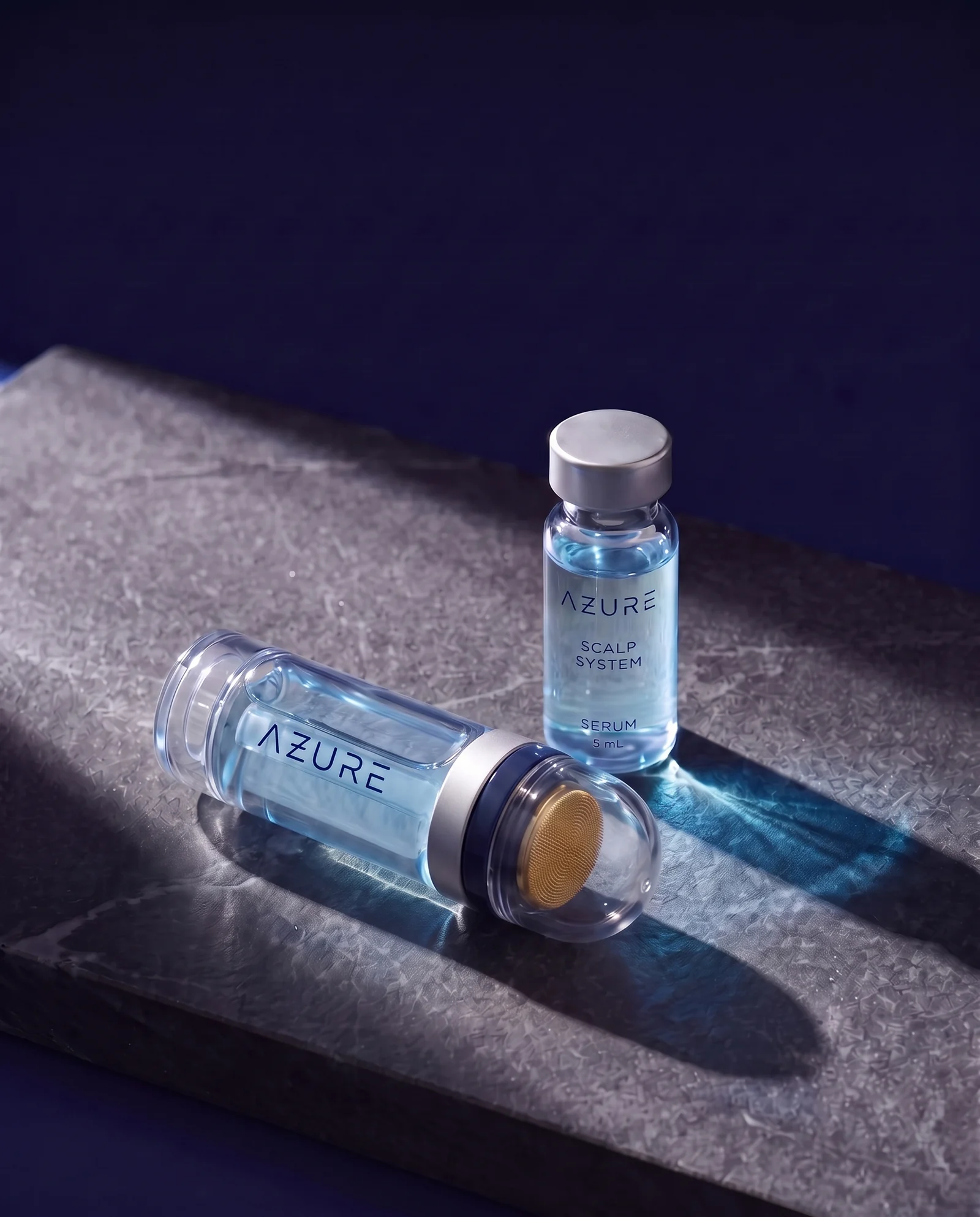 The AZURE applicator lying on dark stone beside a vial of blue serum, in raking light